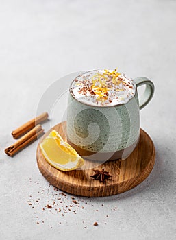 Mug of hot chocolate with whipped cream and orange zest on a wooden board on a light background with a cinnamon sticks and fresh