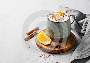 Mug of hot chocolate with whipped cream and orange zest on a wooden board on a light background with a cinnamon sticks, napkin