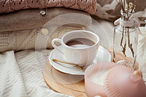 A mug of hot cocoa knitted sweaters a bouquet of white dried flowers in a vase a candle on the bed. Breakfast in bed. Cozy