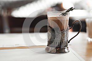 A mug of hot cocoa with a rosemary branch in a vintage metal cup holder. Retro style food photo concept. Blurred