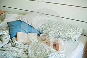 Mug of hot coffee, book, soft slippers on the bed. Breakfast in bed. Cozy home