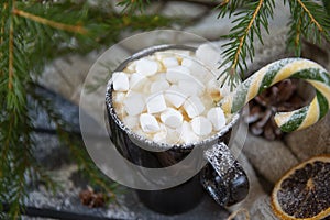 Mug of hot coffee, chocolate with lots of marshmallows and candy,   background of green fir branches, winter hot drink,  Christmas