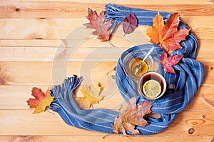 Mug of hot tea, honey, autumn leaves and scarf on wooden background. Top view, copy space
