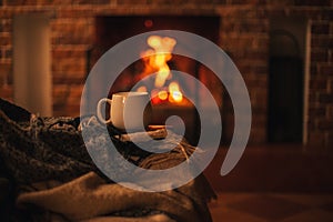 Mug with hot tea standing on a chair with woolen blanket in a cozy living room with fireplace