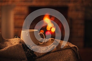 Mug with hot tea standing on a chair with woolen blanket in a cozy living room with fireplace