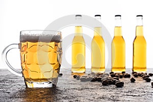 Mug with light beer near bottles and coffee grains on brown textured surface.