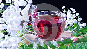 A mug of red tea in white hibiscus flowers and green leaves of medicinal tea on a wooden stand.Zen tea ceremony. Photo of red