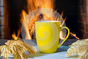 Mug of tea or coffee and autumn leaves before cozy fireplace, in country house