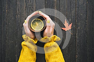 Mug of tea with lemon in a female hand. Wooden background, autum