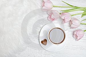 Mug of tea and pink tulips. Light wooden background.