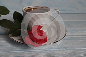 A mug of tea and a red rose on a white saucer.