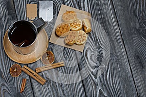 Mug of tea and waffles. Nearby is a bag of tea and spices. On painted boards. Autumn still life