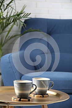 Mugs of coffee with stylish cup coasters on metal table in room