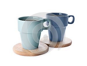 Mugs of coffee and stylish wooden cup coasters on white background