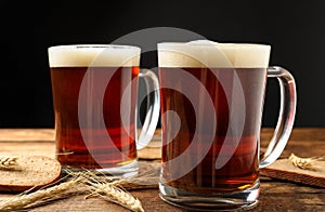 Mugs of delicious kvass, spikes and bread on table against black background