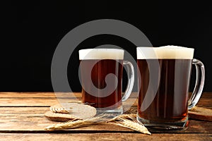 Mugs of delicious kvass, spikes and bread on table against black background. Space for text