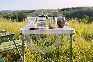 Mugs, grinder, coffee beans on folding table for outdoor camping