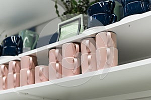 Mugs on shelf on a shelf in retail gift store. Pink and dark blue coffee mugs on shelf in kitchen. Stack of ceramic cups