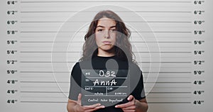 Mugshot of millennial arrested woman with curly hair being photographed in police station. Young female criminal raising