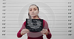 Mugshot of millennial woman with ponytail turning to sides while posing for photo. Portrait of female criminal looking