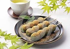 Mugwort-flavored rice dumpling covered with soybean flour and green tea served on a black plate set against a white background