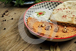 Muhammara is a classic eastren dish. baked pepper and walnut puree with Bazlama and yogurt in a ceramic plate on a wooden