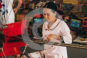 MUI NE, VIETNAM - MARCH 6, 2017: Woman weaver working on a traditional Vietnamese weaving loom for yarn silk