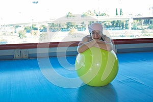 Mujer con una bufanda de cÃÂ¡ncer rosa apoyada en la bola de pilates amarillo en un gimnasio photo