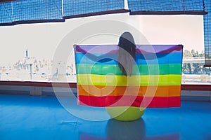 Mujer sentada en pilates amarillo bola sosteniendo la bandera del orgullo gay en un gimnasio photo