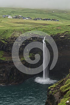 Mulafossur Waterfall view with the countryside houses in the background, Faroe Islands, vertical