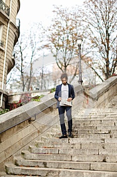 Mulatto guy walking down steps with newspaper.