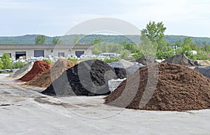 Mulch and gravel piles in front of a packaging plant