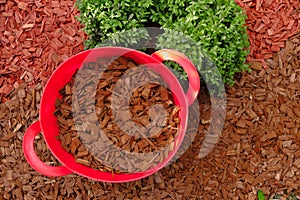 Mulching soil cover made of natural materials.Decorative chips garden.Red chips for mulching in red silicone bucket in a