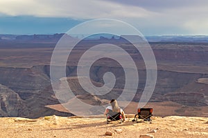 Muley Point - Woman sitting in camping chair enjoying scenic aerial vistas of desert landscape of Valley of the Gods