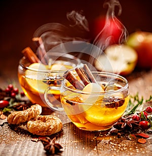 Mulled cider with slice apples, cinnamon, cloves, anise stars and citrus fruits in glass cups on a wooden rustic table, close-up.