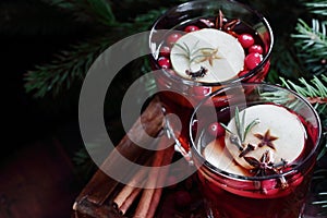 Mulled red wine with cranberry, apple and spices: anise, cinnamon, rosemary and cloves on dark moody black background and fir bran