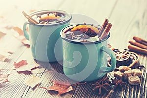 Mulled wine in blue enameled rustic mugs with spices. Autumn leaves on desk.