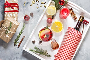 Mulled wine, a bottle of red wine, spruce branches, cinnamon, orange and lemon on white tray on concrete background. Winter drinks