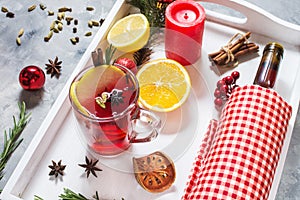 Mulled wine, a bottle of red wine, spruce branches, cinnamon, orange and lemon on white tray on concrete background. Winter drinks