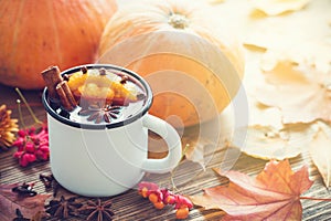 Mulled wine in enameled cup and pumpkins on table with autumn leaves.