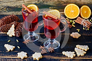 Mulled wine with fresh orange slices and various winter spices on the black wooden background decorated with Christmas cookies