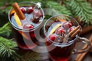 Mulled wine in glass mug with berries, cinnamon sticks and star anise on brown wood table