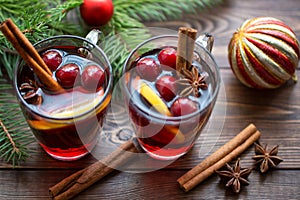 Mulled wine in glass mug with berries, cinnamon sticks and star anise on brown wood table
