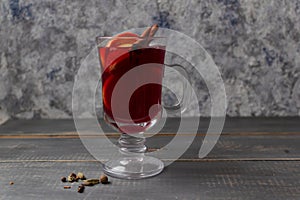 Mulled wine in a glass mug with cinnamon and oranges on a wooden gray table