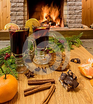 Mulled wine glintwine in drinking glasses and christmas decorations, against cozy fireplace background