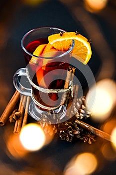 Mulled wine Hot christmas drink with spices on a dark background. Orange slices, cinnamon sticks, christmas cones, bright bokeh.