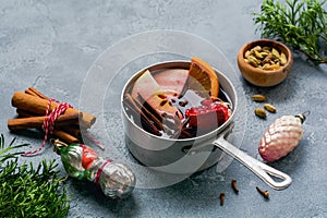 Mulled wine hot drink with citrus, apple, pomegranate and spices in aluminum casserole with vintage Ð¡hristmas tree