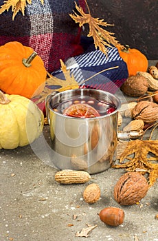 Mulled wine in metal rustic mug with spices and citrus fruits decorated with autumn leaves and pumpkin