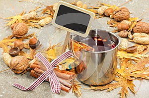 Mulled wine in metal rustic mug with spices and citrus fruits decorated with autumn leaves and pumpkin