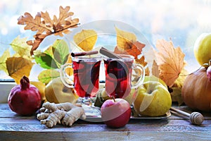 Mulled wine, organic fruits, autumn leaves, spices on a wooden table against the background of a window